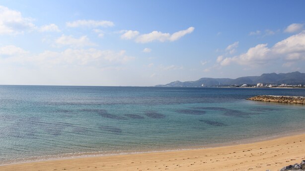 A beach with clear water, a sandy shore, and distant mountains.