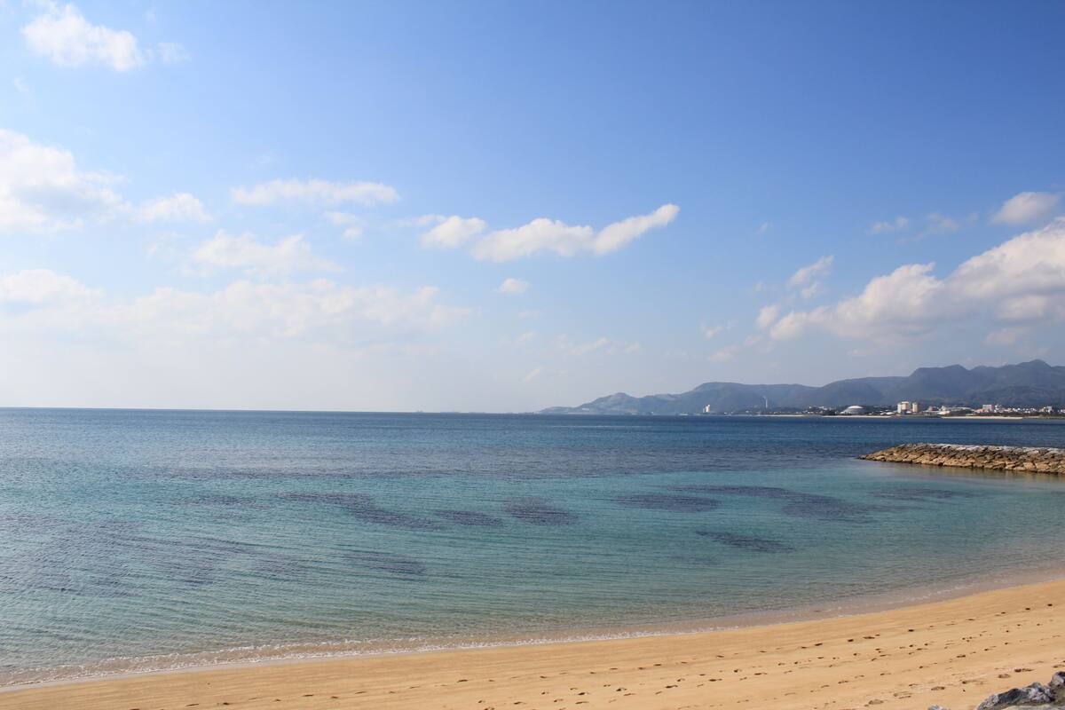 A beach with clear water, a sandy shore, and distant mountains.