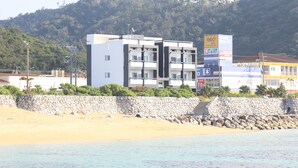 A modern hotel with multiple floors, a stone wall in front, and a beach in the background.