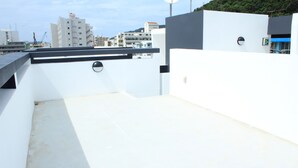 A rooftop terrace with a flat surface, a circular window, and a partial view of buildings in the background.