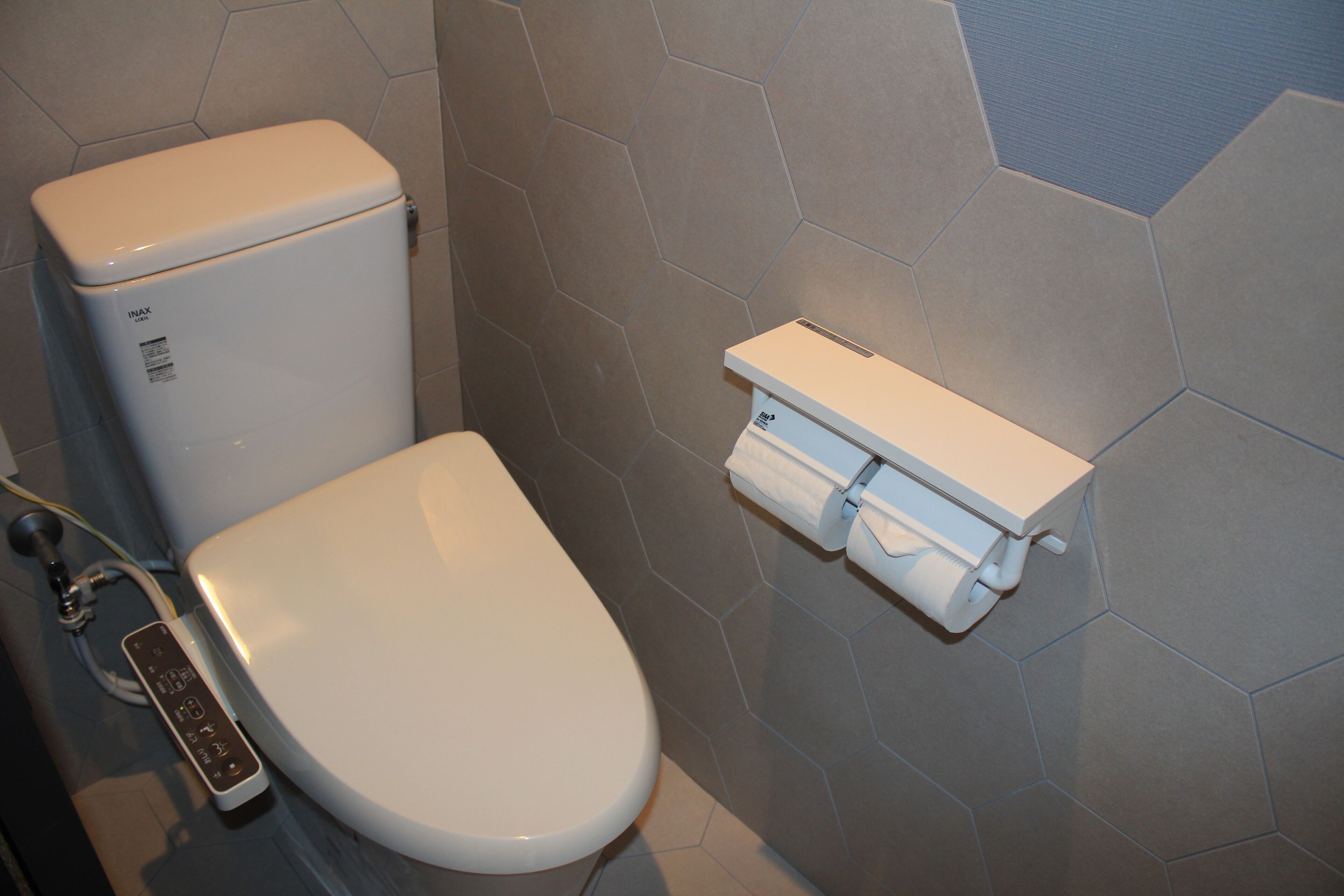 A modern bathroom with a toilet, a toilet paper holder, and a control panel.