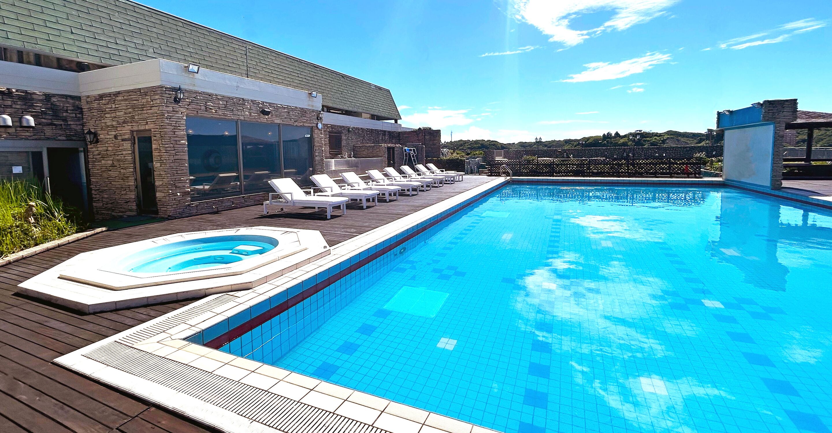 Uma piscina com espreguiçadeiras, uma banheira de hidromassagem e um deck de madeira.