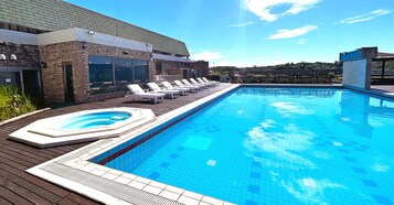 Una piscina con sillas de descanso, un jacuzzi y una terraza de madera.
