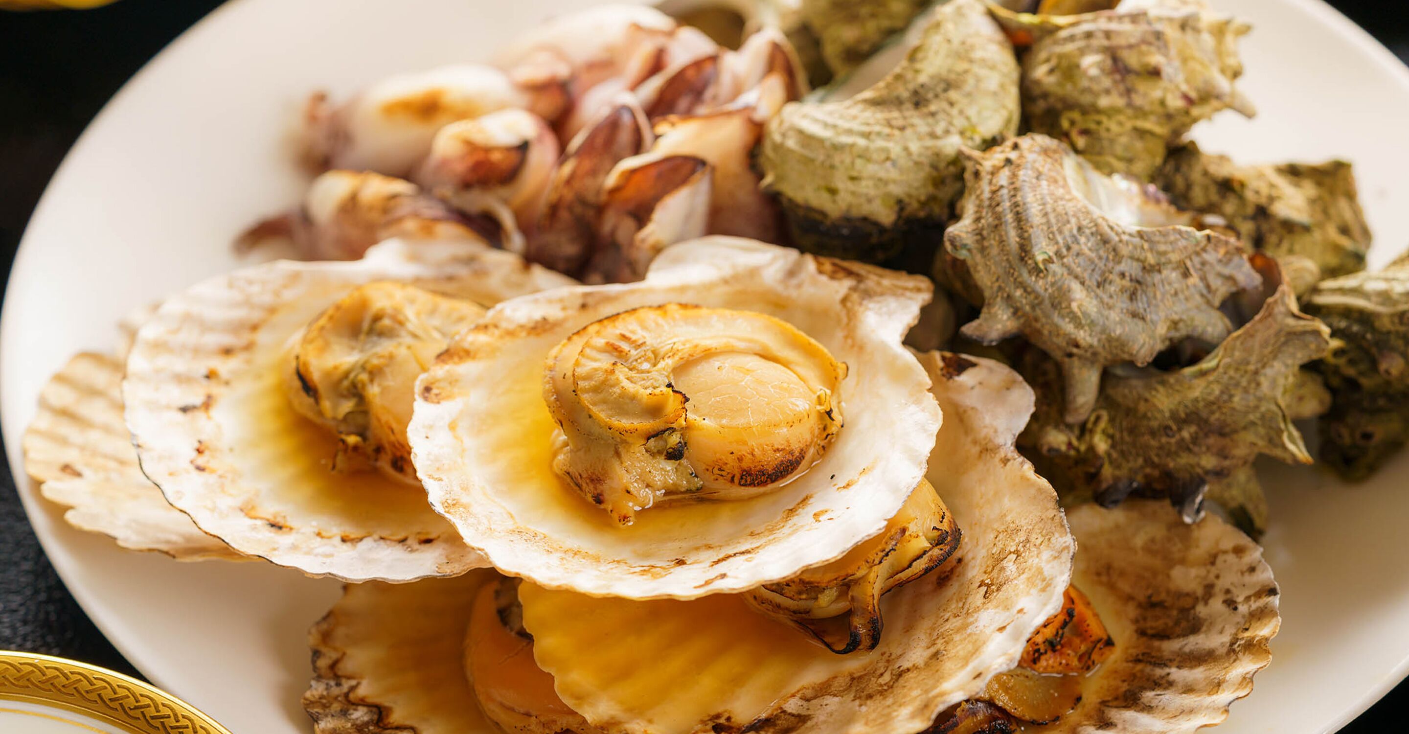 Un plato de vieiras cocinadas y diversos tipos de mariscos.