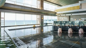 Uma área de piscina interior ampla com vista para o mar, um bar com várias garrafas e um teto alto com vigas aparentes.