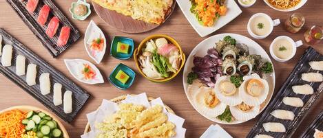A variety of Japanese dishes including sushi, tempura, and noodles, arranged on a wooden table.