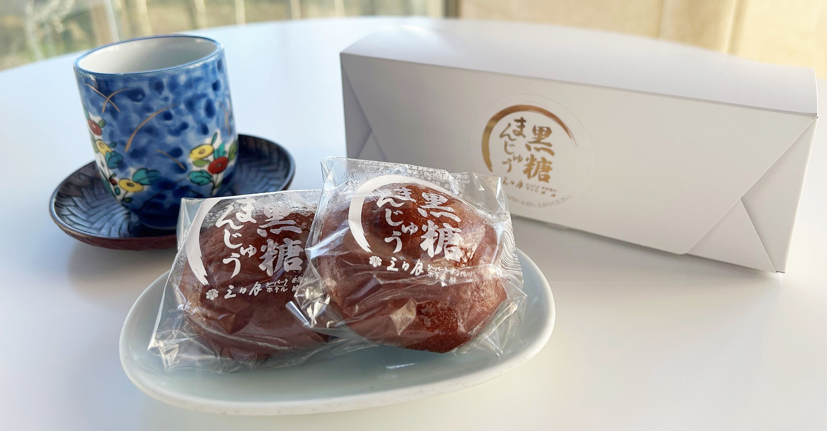 A table with a blue ceramic cup, a white box with Japanese text, and two packaged items on a plate.