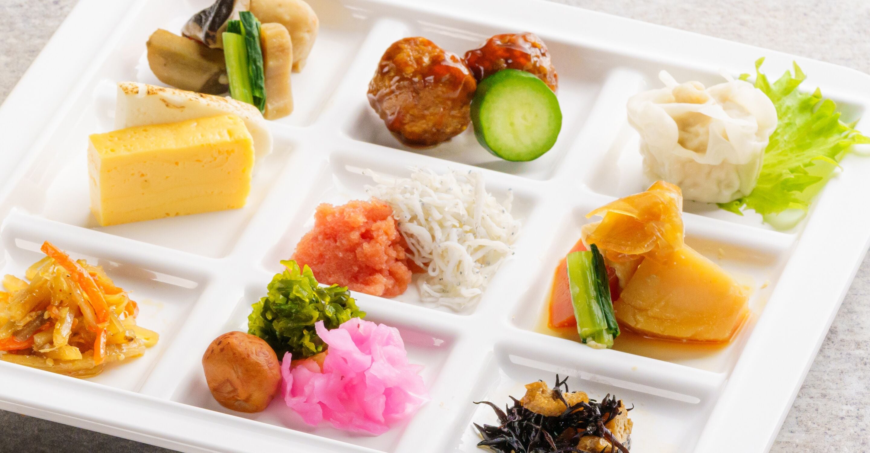 Una bandeja rectangular blanca dividida en varios compartimentos que contienen diferentes platos.