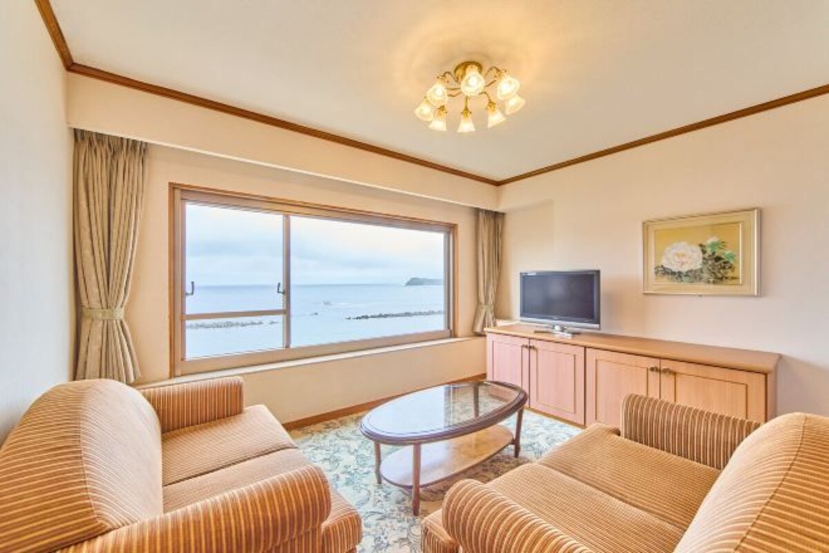 A hotel room with a large window, a television, a sofa, and a small table.