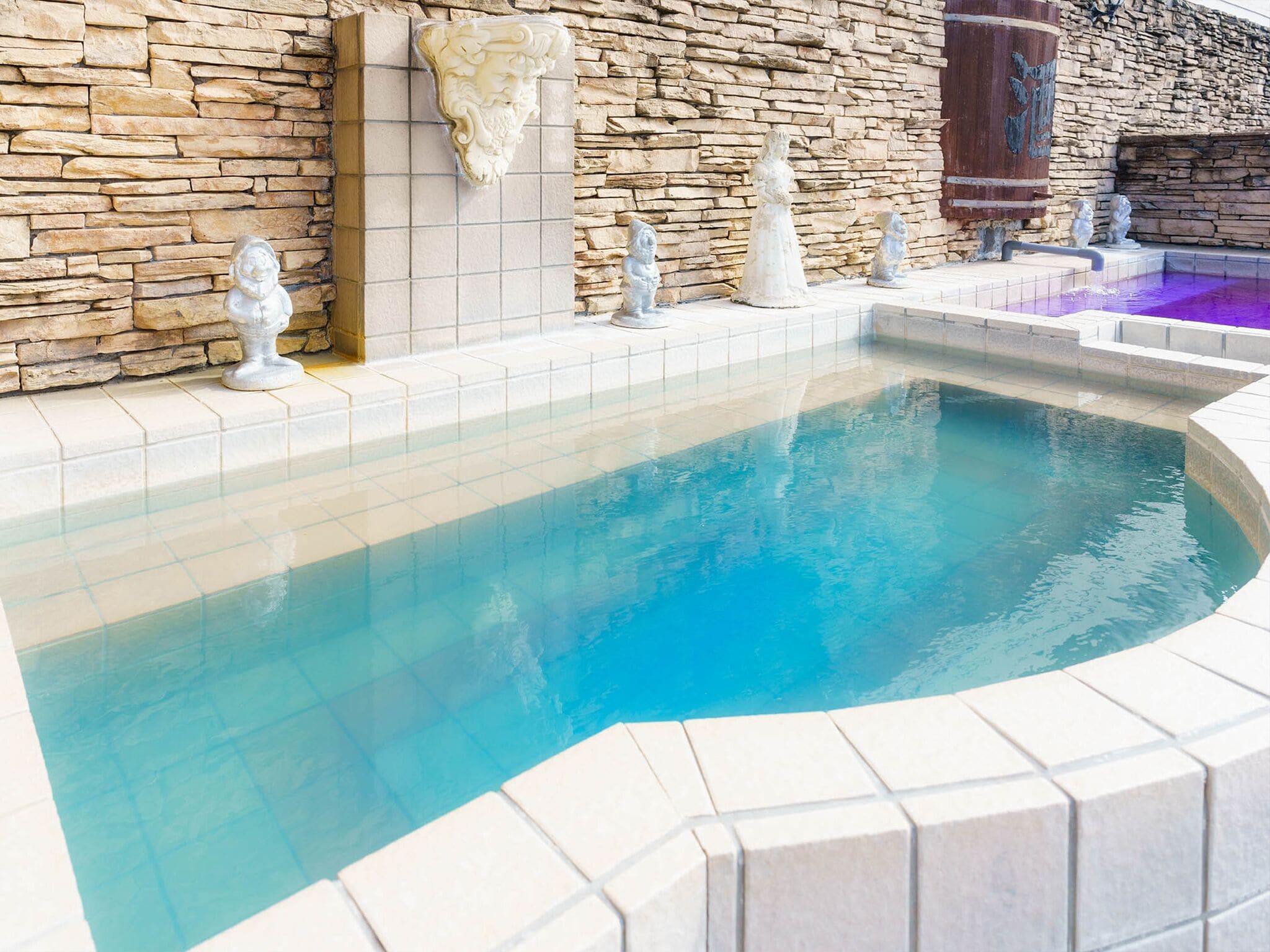 A swimming pool with stone walls and decorative statues.