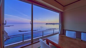 Quarto com uma janela ampla de frente para o mar tranquilo e um litoral rochoso.