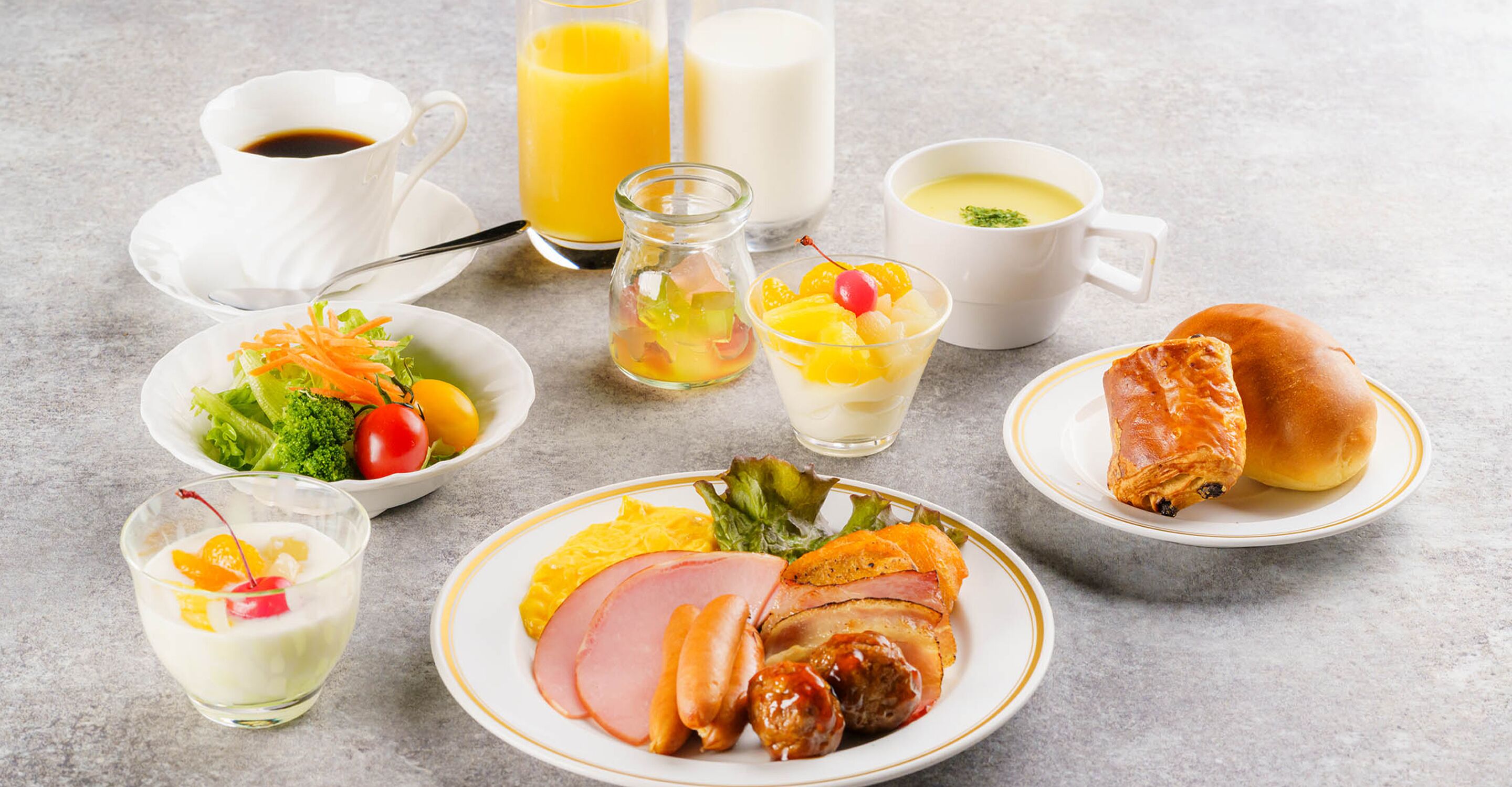 Un desayuno con diferentes platillos, como huevos, jamón y tostadas, además de bebidas como jugo de naranja y café.