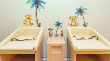 Deux lits de taille enfant, séparés par un paravent en bois, et chacun orné d’un petit autocollant représentant un animal sur le mur au-dessus.