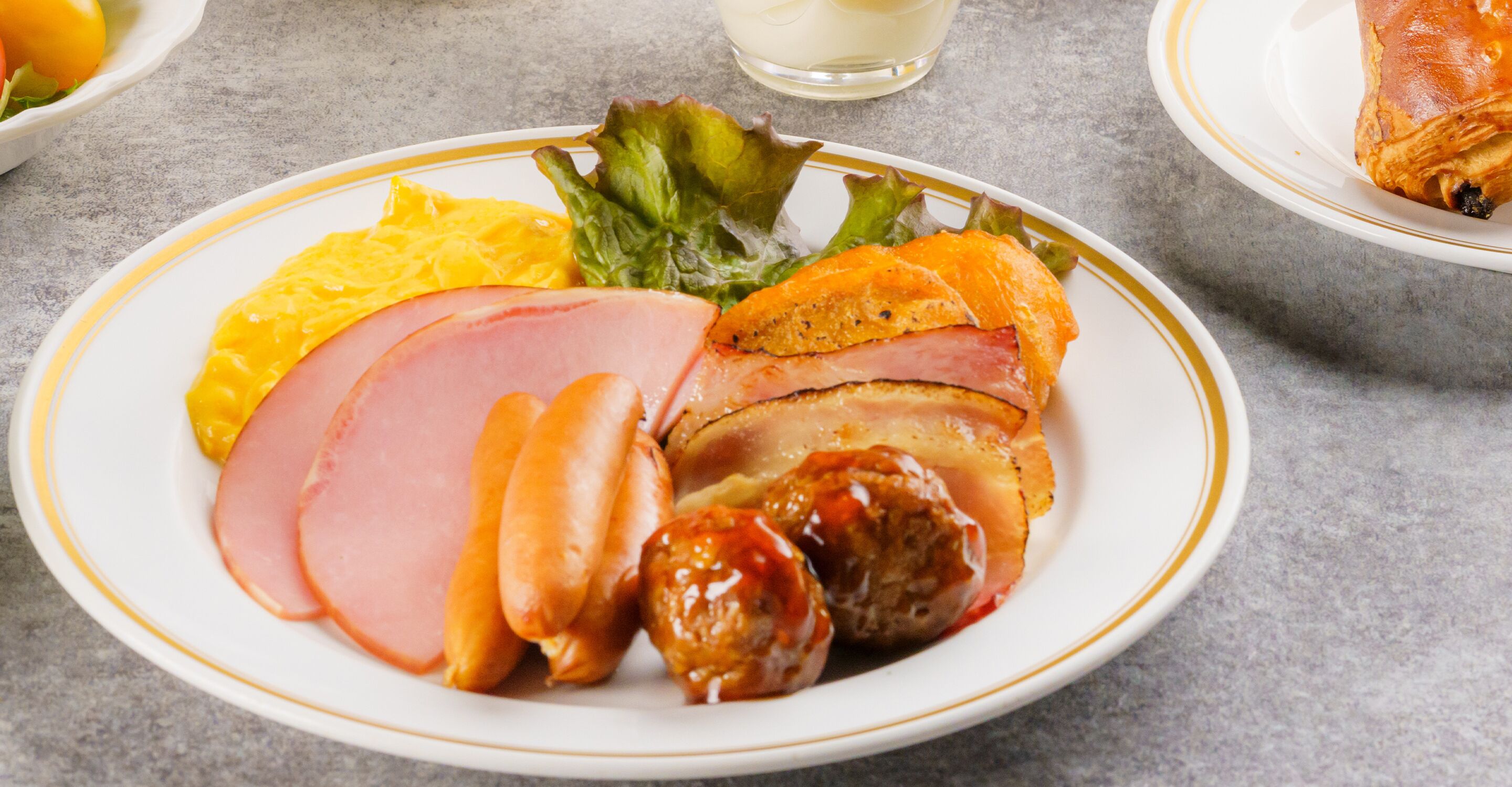 A plate of food with ham, sausages, and a side of vegetables.