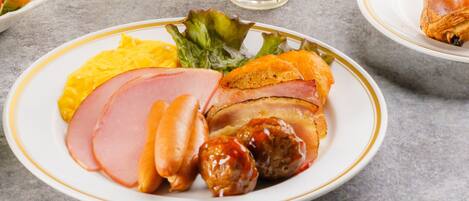 A plate of food with ham, sausages, and a side of vegetables.