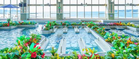 Una piscina con múltiples carriles, rodeada de coloridas parterres y amplias ventanas que ofrecen vistas al mar.