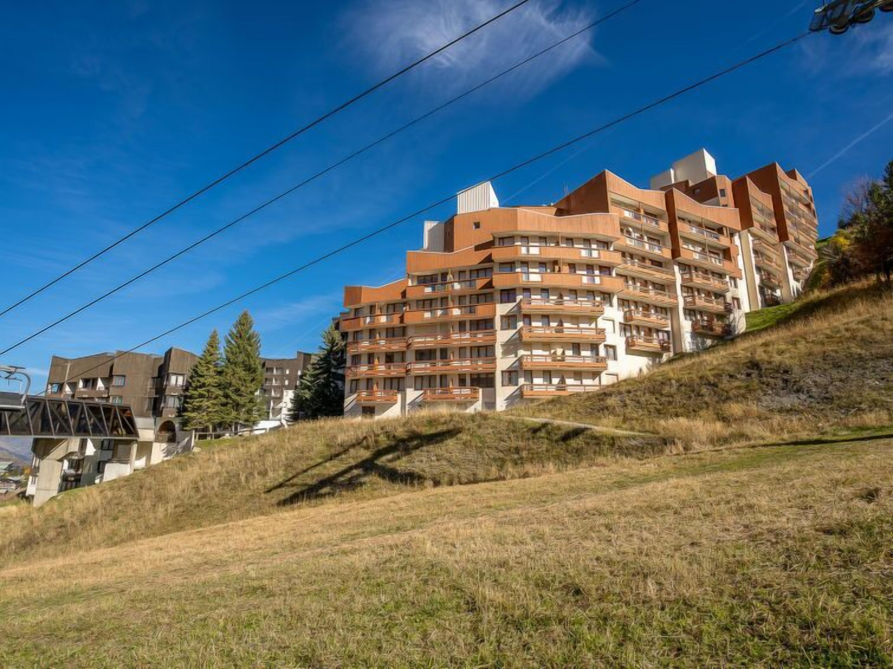 En flervåningsbostadsbyggnad med balkonger, belägen på en sluttning med klar himmel.