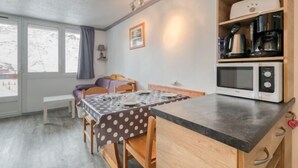 Ein gemütliches Zimmer mit Esstisch, Stühlen, einer Mikrowelle und einem Regal mit Küchengeräten.