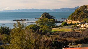 A coastal landscape with a view of the sea, mountains in the distance, and a residential area with houses and greenery. - Beach House on the Ridge - Kaiteriteri House (Little Kaiteriteri)