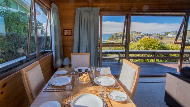 A wooden dining table set with plates, glasses, and a bowl of bread. - Beach House on the Ridge - Kaiteriteri House (Little Kaiteriteri)