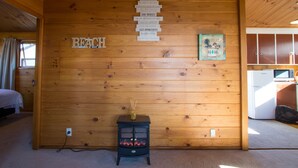 A wooden cabin interior with a wall-mounted sign listing life rules, a small table with a candle, and a kitchenette area. - Beach House on the Ridge - Kaiteriteri House (Little Kaiteriteri)