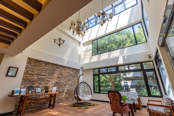 A spacious room with a high ceiling, a hanging chair, a table with a plant, and large windows offering a view of greenery outside. - Jimei Rustic Homestay (Ji'an)