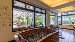 A room with a foosball table, large windows, and a view of the outside patio area. - Jimei Rustic Homestay (Ji'an)