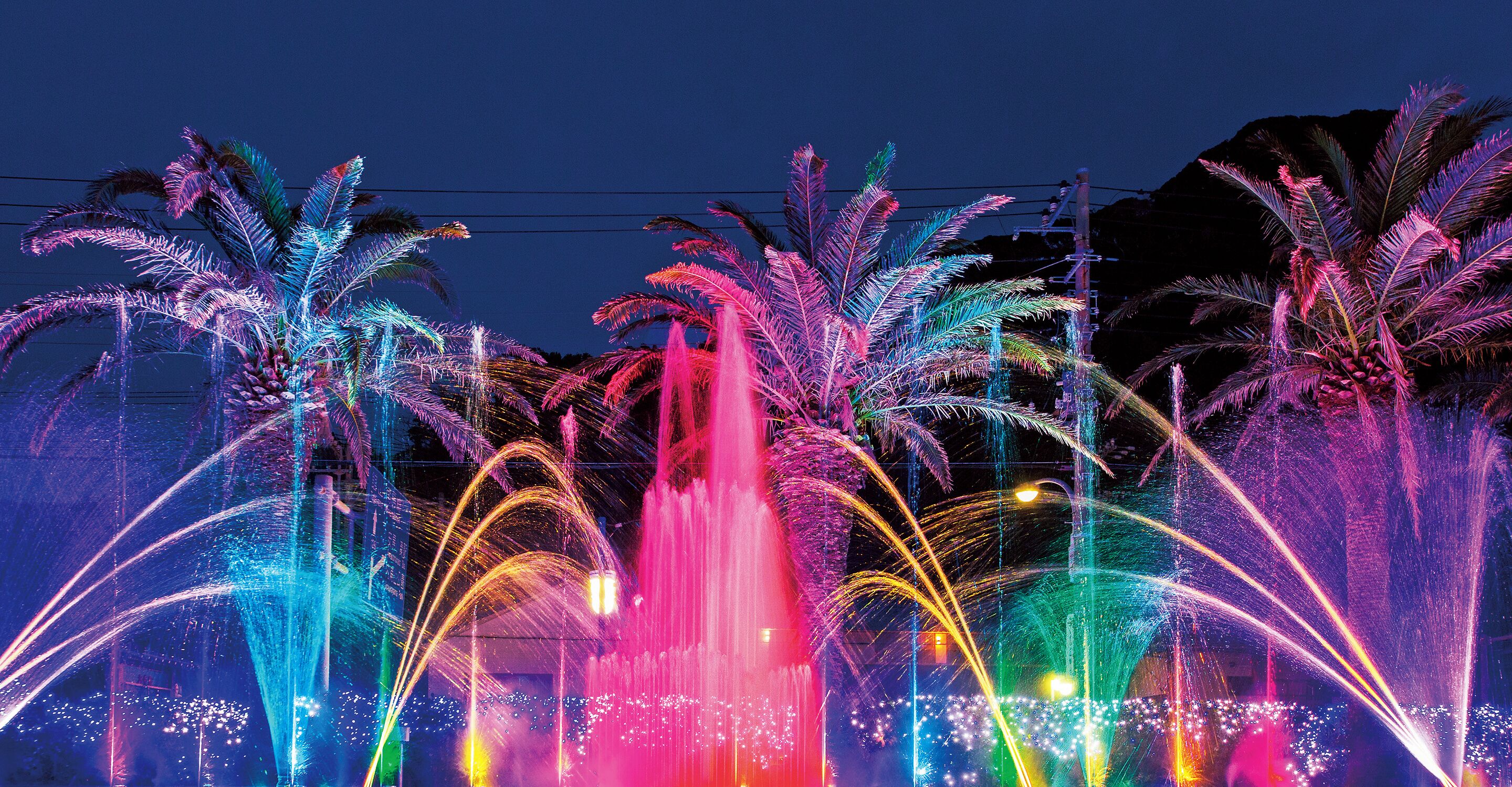 Escena nocturna con fuentes de agua y palmeras.
