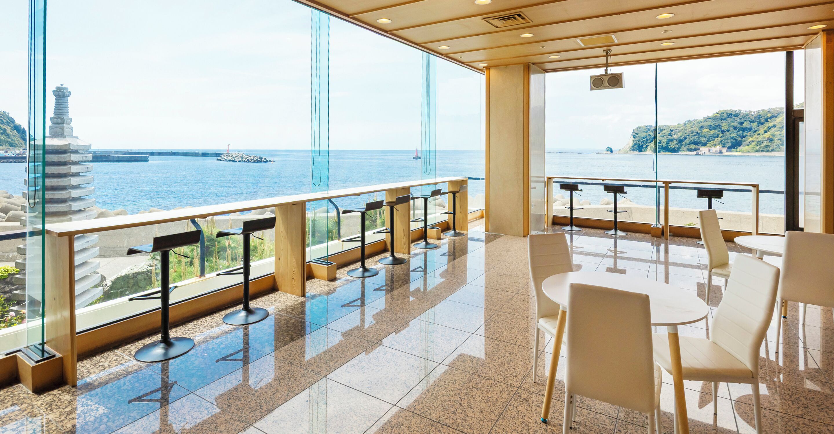 Un interior moderno con vistas al mar, que incluye una zona de bar con taburetes y un espacio de estar con mesas y sillas.