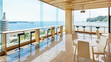 Un interior moderno con vistas al mar, que incluye una zona de bar con taburetes y un espacio de estar con mesas y sillas.