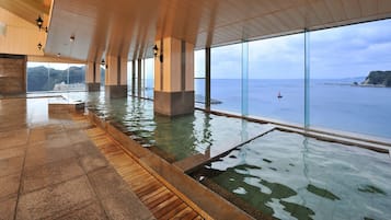 Ein großzügiger Innenpoolbereich mit freiem Blick auf das Meer und eine hügelige Landschaft.