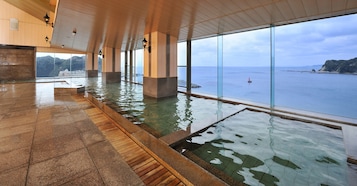 A spacious indoor pool area with clear views of the sea and a hilly landscape.