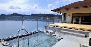 A hot spring area with a wooden deck and stone steps leading to a pool, overlooking a body of water and distant hills. - Mikazuki Sea-Park Hotel Awa Kamogawa (Kamogawa)