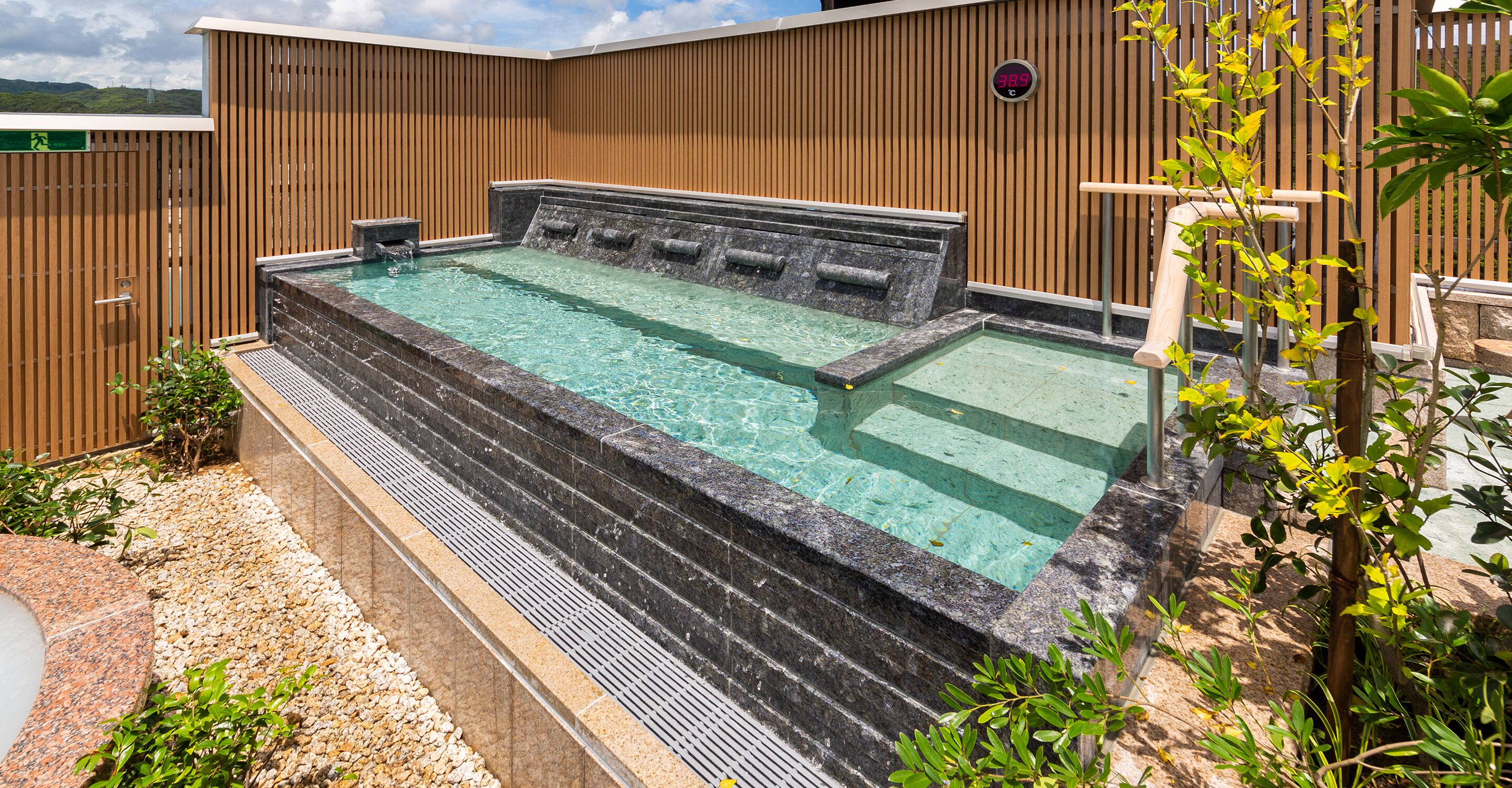 A hot tub with steps leading into it, surrounded by a wooden fence and greenery.