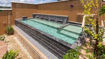 A hot tub with steps leading into it, surrounded by a wooden fence and greenery.