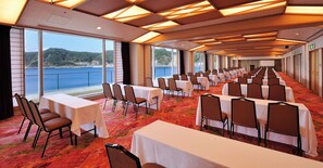 A conference room with tables and chairs arranged for a meeting, large windows offering a view of the sea, and a ceiling with wooden beams. - Mikazuki Sea-Park Hotel Awa Kamogawa (Kamogawa)