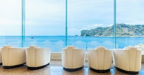 A row of white armchairs facing a large window with a view of the sea and a distant island. - Mikazuki Sea-Park Hotel Awa Kamogawa (Kamogawa)