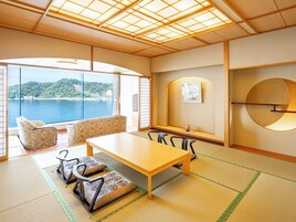 Una habitación japonesa tradicional con suelo de tatami, una mesa baja y sillas. Un ventanal ofrece vistas a una masa de agua y vegetación.