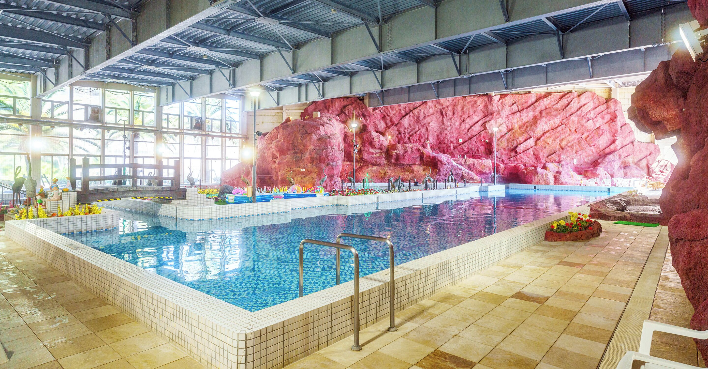 Una piscina interior con suelo de baldosas, una escalera de piscina y un muro de roca de fondo.