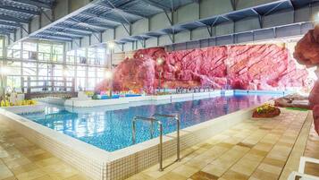 Una piscina interior con suelo de baldosas, una escalera de piscina y un muro de roca de fondo.