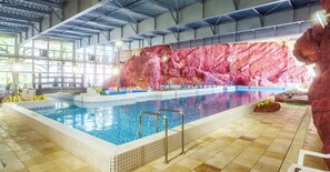 Une piscine intérieure avec un sol carrelé, un escalier d’accès et un mur de fond en pierre.