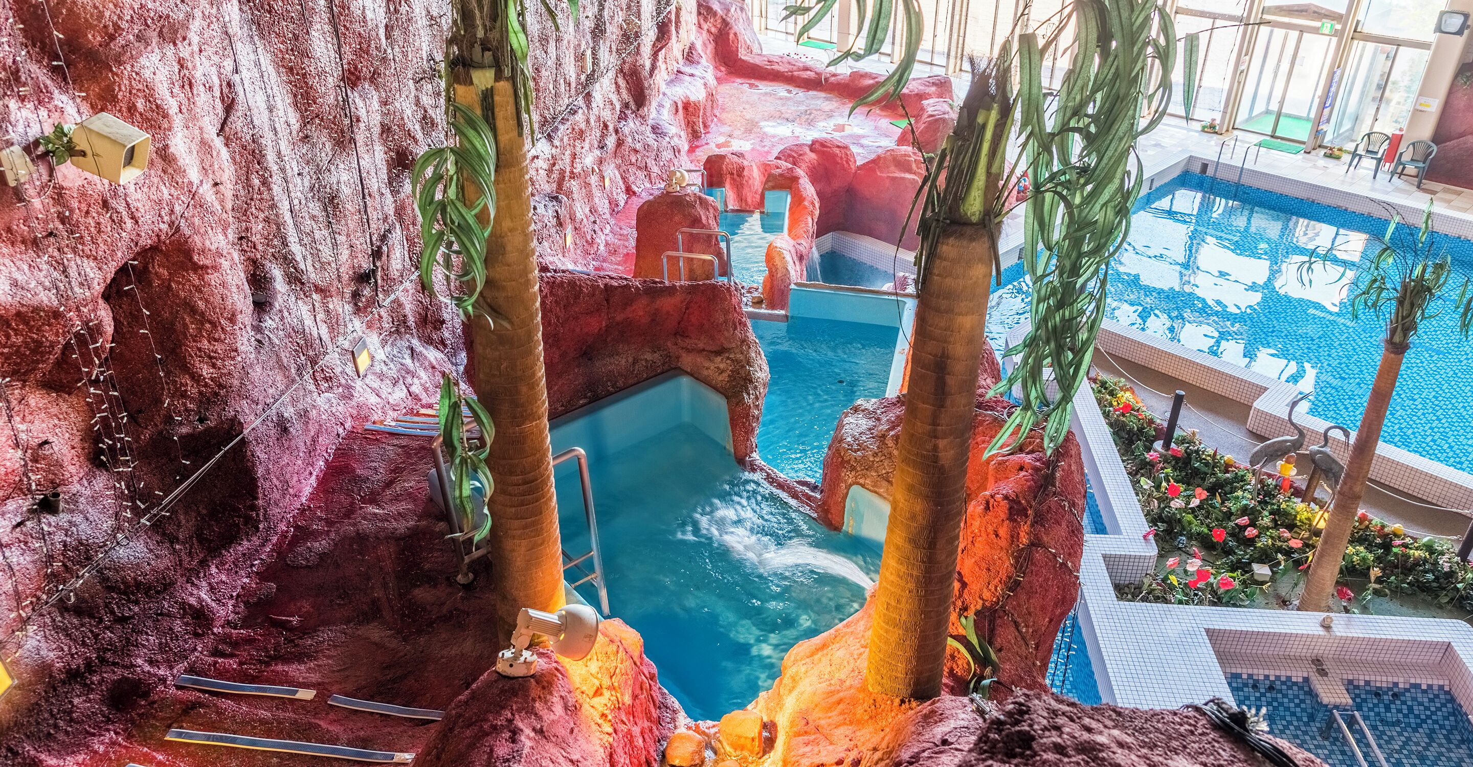 An indoor pool with a rocky landscape and palm trees.
