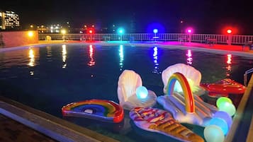 Une piscine illuminée de lumières colorées la nuit, avec des jeux gonflables flottant à la surface.