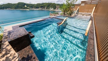 Ein Pool mit klarem Wasser, Holzstufen und Blick aufs Meer.