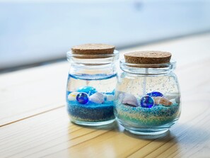 Two glass jars with cork lids containing blue sand, seashells, and decorative stones on a wooden surface. - Mikazuki Sea-Park Hotel Awa Kamogawa (Kamogawa)