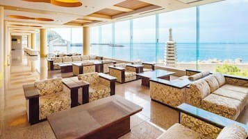 Un amplio salón con múltiples opciones de asientos, ventanas grandes que ofrecen vistas al océano y una decoración de diseño moderno.