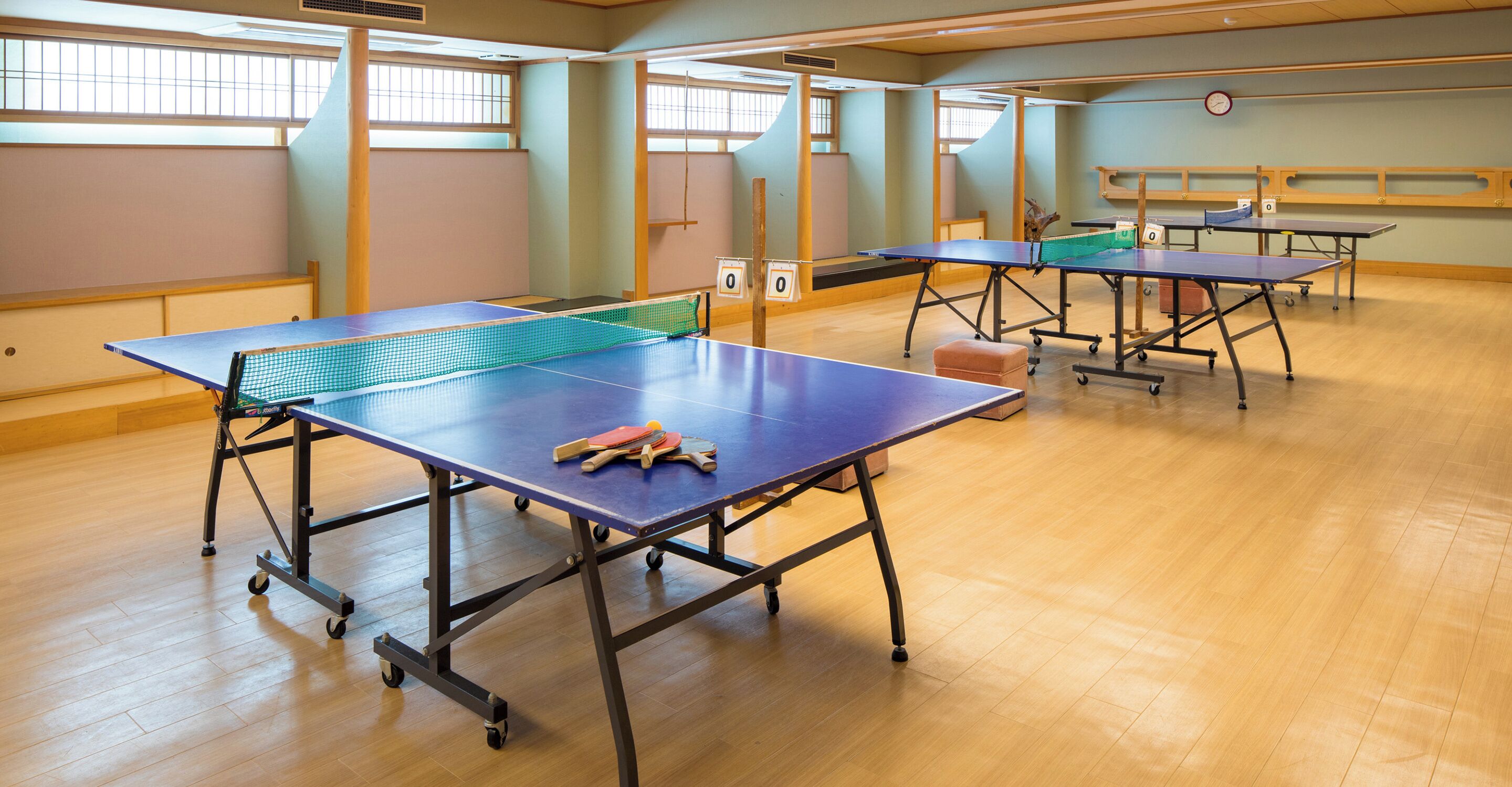 A room with multiple ping pong tables, each with a net and paddles, and a clock on the wall.