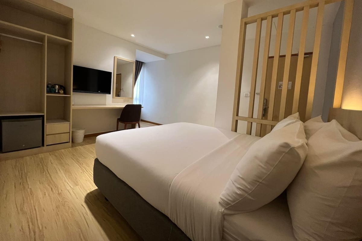 A hotel room with a large bed, a desk, a chair, a television, and a wardrobe.