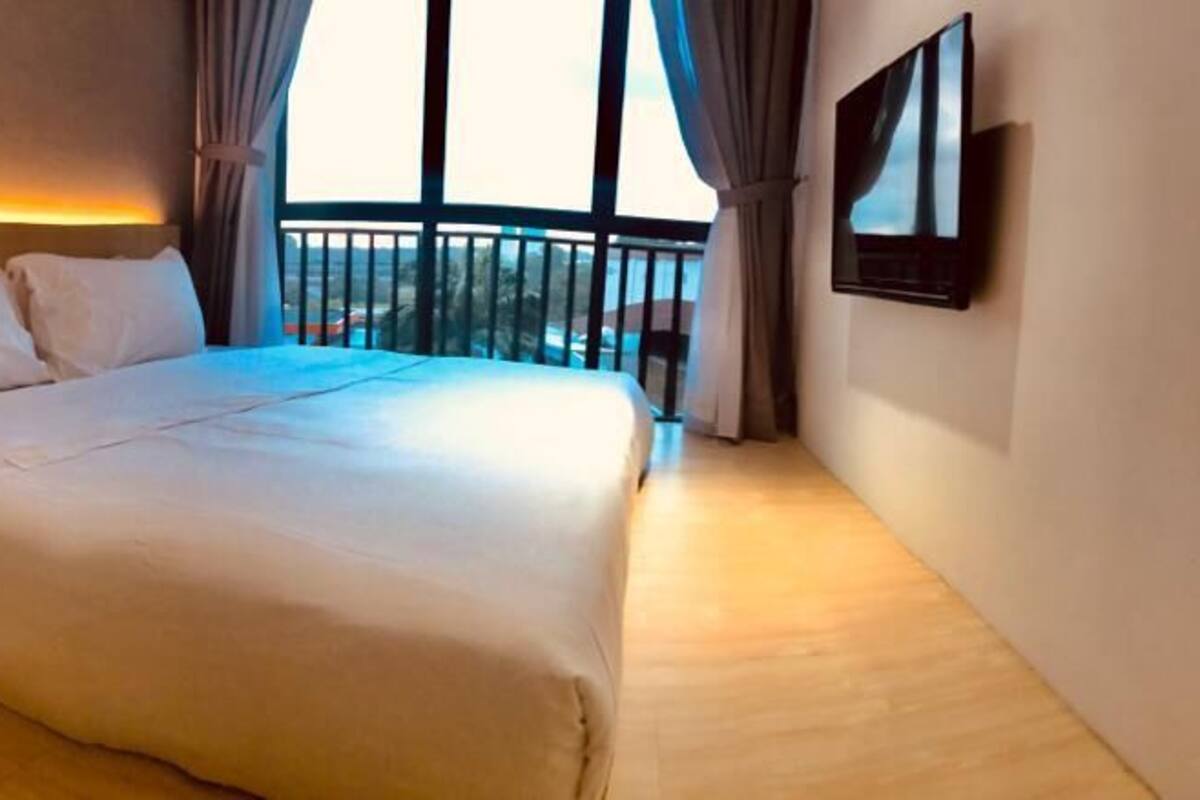 A hotel room with a large bed, a bedside table with a phone, a TV mounted on the wall, and a balcony with a railing.