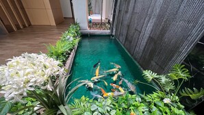 A koi pond with various fish, surrounded by lush greenery and white flowers. - Miyabi Hotel (Masai)